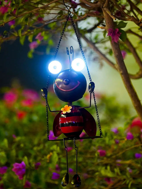 Solar Powered Ladybug Swing Garden Decor Waterproof Metal Hanging Lights glowing at night in garden setting with flowers.