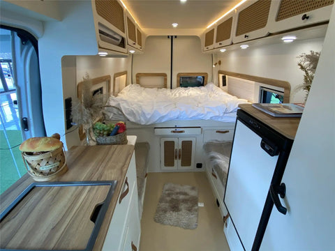Interior view of an RV camper featuring rotating aluminum table legs for RV campers setup, with a kitchen and bedding.