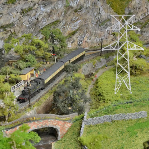 Totally Legit N Scale 1 160 Miniature Electric Transmission Tower near train set and scenic landscape display.