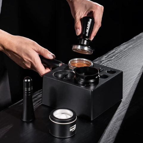 Top Shelf Espresso Barista Gear Featuring 54 Mm Stainless Steel Tamper Fits Breville Portafilters Includes Precision Wdt Needles Sleek Dosing Funnel And Two Hundred Premium Paper Filters To Nail That Perfect Morning Pull. Hands using a stainless steel tamper above a breville portafilter on a black wooden surface.