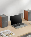 R1280T Powered Bookshelf Speakers with wooden enclosure, laptop, and remote on a desk setup for home office