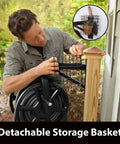 Man attaching detachable storage basket to wall post beside garden, showcasing Multi Directional Garden Hose Reel with 360 Degree Rotation.