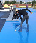 Workers applying Rock Solid Self Adhesive Waterproof Membrane Roll on a blue roof surface using a roller and smoothing technique.