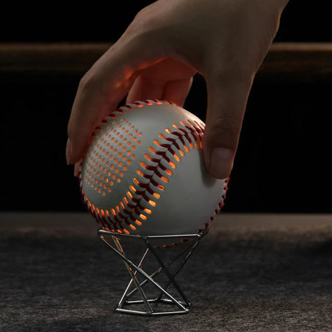 Hand placing baseball on Rose Gold Premium Metal Baseball Display Stand for Baseballs Tennis Balls Golf Balls and Collectibles Sturdy Stainless Steel Holder Sleek Gold Finish Perfect For Showpieces and Party Decor.