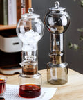 Premium Glass Cold Brew Drip Tower With Adjustable Flow Dripper For Smooth Cold Extraction Coffee Maker 600 Milliliter Gray Body on table with ice and brewed coffee.