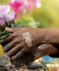 Hand wearing waterproof clear bandage with 360 degree seal while gardening, protecting minor wounds from dirt and germs.