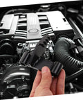 FELTECHELECTR flywheel holding tool held in hand in a car engine bay; black metal bracket