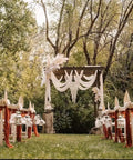 Outdoor wedding aisle with chairs and hanging drapes on a wooden arch in a wooded setting