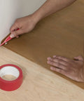 Trimming waxed paper underlayment with red knife during wood floor installation; Waxed Paper Underlayment For Wood Flooring 3 Ft By 250 Ft Roll 750 Sq Ft 30 Lb Pro Grade Heavy Duty Kraft Paper Moisture Barrier To Ease Nail Down Installations And Minimize Squeaks visible.