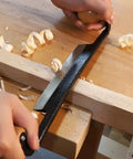 Straight Draw Knife Woodworking Shaving Tool Featuring Heavy Duty Steel Blade And Grippy Wooden Handle For No Sweat Bark Stripping Log Peeling And Quick Finishing Work in use with wood shavings on table.