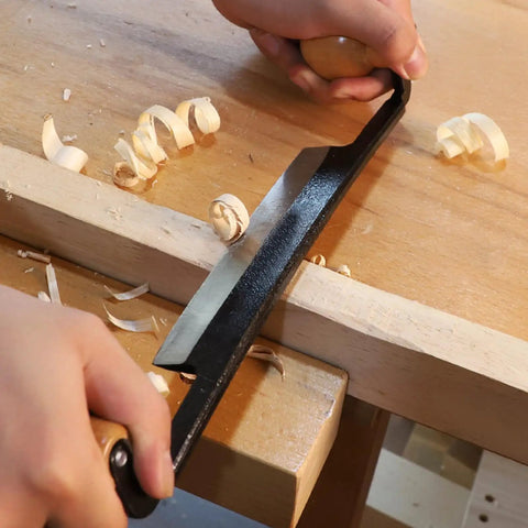Straight Draw Knife Woodworking Shaving Tool Featuring Heavy Duty Steel Blade And Grippy Wooden Handle For No Sweat Bark Stripping Log Peeling And Quick Finishing Work in use with wood shavings on table.