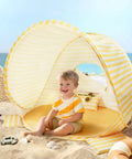 Child sitting in a Pop Up Baby Beach Tent With 2026 Upgraded UV Protection Lightweight Portable Sun Shelter For Babies on the sand