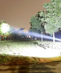Person using Beast Mode Bright 90000 Lumen Hunting Headlamp With 9 Core Wide Beam, illuminating trees at night on a grassy field.
