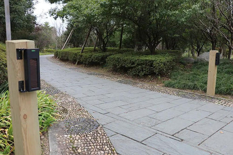 Solar Wireless Outdoor Photoelectric 2 Beam Sensor IP66 Waterproof Driveway Alarm installed along a forested path.