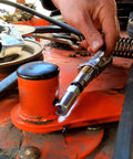 Push-on slotted right-angle grease coupler held by hand, chrome metal, on orange workbench.