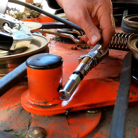 Push-on slotted right-angle grease coupler held by hand, chrome metal, on orange workbench.