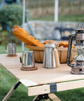Outdoor scene with wooden table set with lantern, mugs, bread, and basket, showing corner edge. Focus keyword: 36 Pack Silicone Corner Protectors For Sharp Furniture Edges With High Elasticity Easy To Install And Remove Peel And Stick Safety Guards To Prevent Kids And Pets From Getting Hurt.