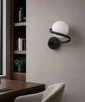 MAHGNTKCX Black Wall Sconce with Opal Glass Globe and Spiral Metal Frame mounted on a wall beside a desk.