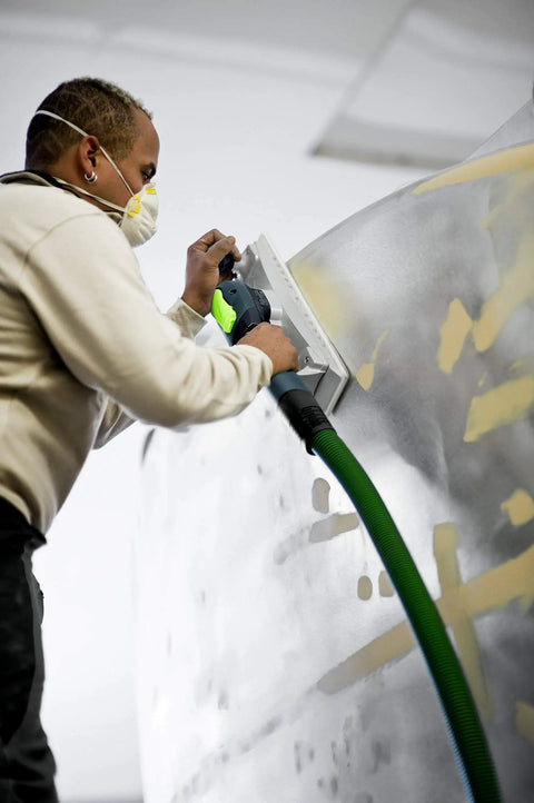 Man using Dust Busting Vacuum Enabled Sanding Block 80 By 200 Mm For Handheld Smoothing on a curved surface with dust extraction hose.