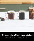 Three glass cups showing classic, rich, and iced coffee brewed styles with scoop of ground coffee in kitchen setting.
