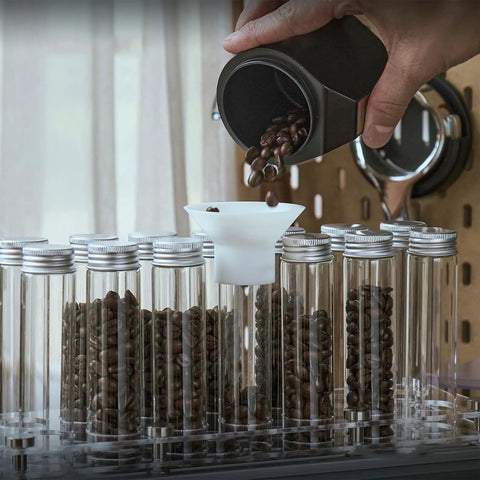 14 Piece Airtight Glass Coffee Bean Storage Tubes With Solid Stand And Hopper Featuring One Way Exhaust Valve Keeps Your Daily Grind Pretty Slick For That Weekend Home Bar Session Countertop Flex, pouring coffee beans into a clear tube.