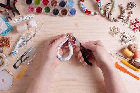 Hands using pliers from 19 Piece Jewelry Making Tools Kit With Zipper Storage Case For Crafting And Repair Perfect DIY Beading And Wirework Set For Beginners And Pros At Home, surrounded by beads and tools.