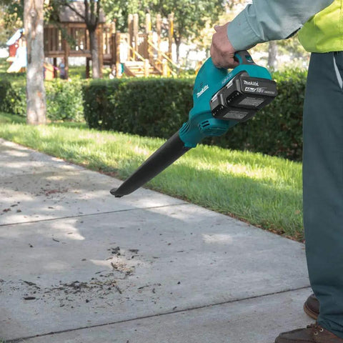 User holding Badass 36V Cordless Leaf Blower Kit with two 18V batteries clearing debris off sidewalk in a park.