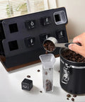 Coffee Bar Game Changer Clear Airtight Bean Storage Jars On Solid Walnut Base Heavy Duty Steel Frame Rack With Six Tubes And Two Funnels Real Deal Countertop Bean Keeper filled with coffee beans and measuring scoop.
