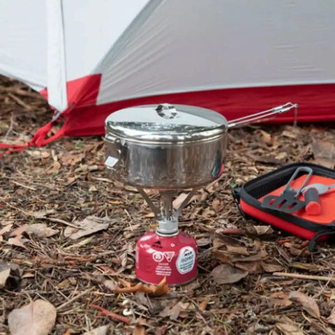 Beefy Stainless Steel Stowaway Camping Pot 475 mL with locking lid on portable stove next to a tent in forest setting