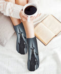 Person wearing witch-themed socks while holding coffee on bed