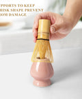 Hand placing bamboo whisk on pink ceramic holder from Pink Matcha Whisk Set With Chasen Holder And Ceramic Stand Includes Bamboo Scoop Fine Mesh Sifter And Tea Tools For Ceremony Gift For Home Barista Vibes And Everyday Froth