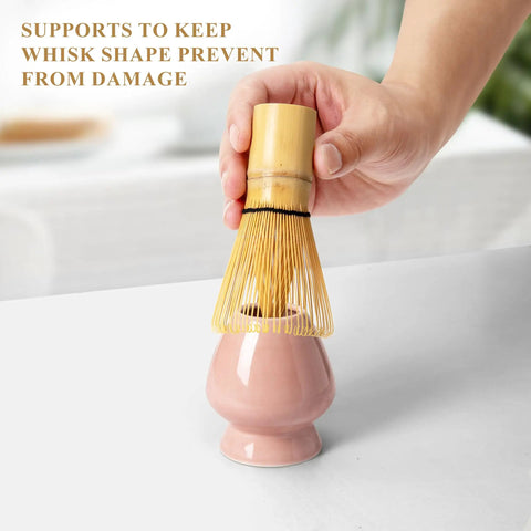 Hand placing bamboo whisk on pink ceramic holder from Pink Matcha Whisk Set With Chasen Holder And Ceramic Stand Includes Bamboo Scoop Fine Mesh Sifter And Tea Tools For Ceremony Gift For Home Barista Vibes And Everyday Froth
