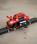 Super Cool CNC Electric Winch For RC Crawler Trucks With Metal Hook Perfect For Rock Gardens And Tricky Terrain Workshop Builds To Crush Scale Rig Challenges, red metallic design, steel cable and hook.