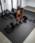 Interlocking 12 Tile Exercise Mat Set For Your Home Gym Setup With 24 By 24 Inch EVA Foam Flooring Puzzle Mats For Safe Workout Area And Equipment Protection Black shown in a gym with weights.