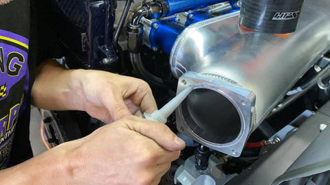 Close-up of a person applying Permatex Ultra Grey RTV gasket maker to a metal engine intake flange.