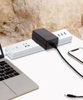 Universal 15V 1.5A Power Adapter With Interchangeable DC Plugs next to laptop and smartphone on white desk