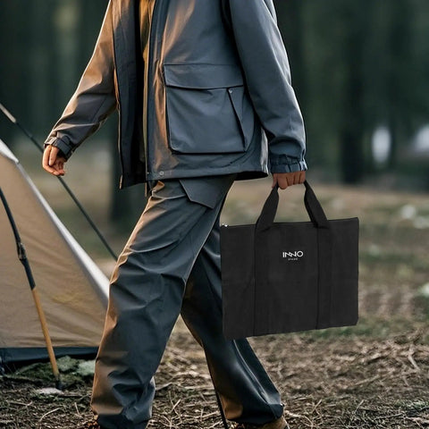 Person carrying tote bag with Collapsible 23 Inch Wood Burning Fire Pit For Camping And Patio near a tent