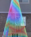 Colorful LED light display in a conical Christmas tree shape illuminated at night in a backyard.