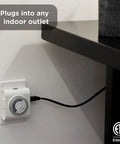 24-Hour Mechanical Outlet Timer Switch With Dual Grounded Plugs installed in an indoor wall socket behind a black shelf.
