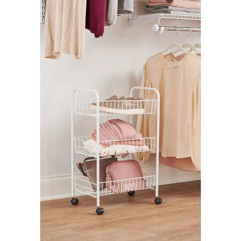 Three Tier Wheeled Wire Shelving Cart With Adjustable Metal Shelves in a bedroom, holding clothes and bags, white finish.