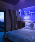 Bedroom with blue neon sign 'Be Kind' above bed, modern decor with indirect lighting creating a cozy atmosphere.