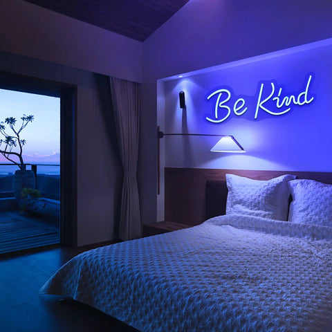 Bedroom with blue neon sign 'Be Kind' above bed, modern decor with indirect lighting creating a cozy atmosphere.