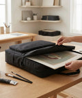 Person placing artwork into black carrying case on wooden table, room with art supplies visible, featuring rugged solar panel carrying case