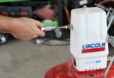 Hand attaching hose to Lincoln 917 Pro Grade 50 To 1 Pneumatic Grease Pump for 120 lb drums, showing control valve and branding.