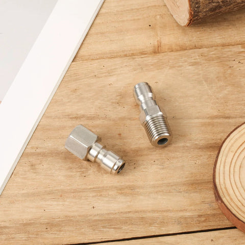 Two stainless steel 1/4-inch quick-connect pressure washer fittings with threaded ends on wooden surface
