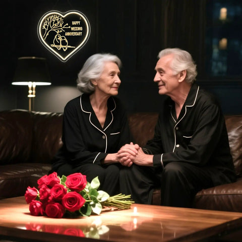 Elderly couple in matching pajamas with a heart-shaped neon sign for wedding anniversary, warm cozy setting with red roses.