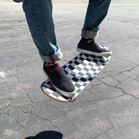 Ultra Sticky 9 By 33 Grip Tape For Longboards, Cruisers And Scooters on a skateboard with checkerboard pattern in use outdoors.