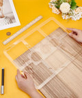 Clear Acrylic Nine Pocket Router Jig And Tracing Template For Woodworking Shops held over a wood surface, with a ruler and pens.