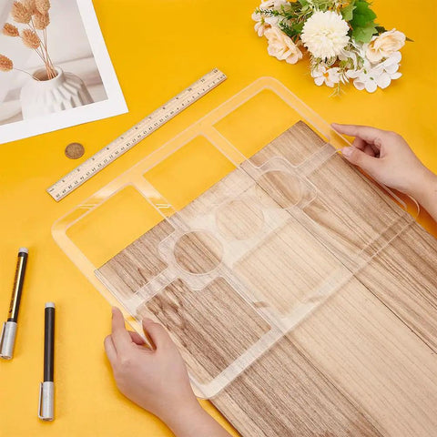Clear Acrylic Nine Pocket Router Jig And Tracing Template For Woodworking Shops held over a wood surface, with a ruler and pens.