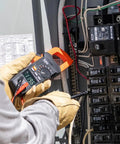 Electrician using Auto Ranging Digital Clamp Meter With True RMS for AC and DC current in electrical panel.